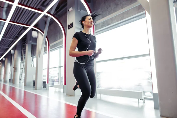 Mujer con auriculares corriendo en pista cubierta en el gimnasio — Foto de Stock