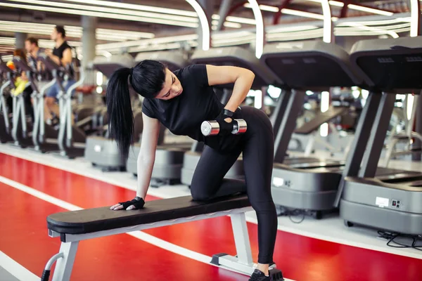 Mujer flexionando los músculos con mancuerna en el banco en el gimnasio — Foto de Stock