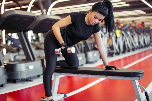 Vrouw flexing spieren met halter op bank in de sportschool — Stockfoto