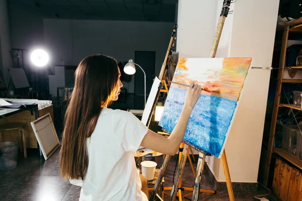 Mujer artista pintando un cuadro sobre caballete con pinturas al óleo en su taller — Foto de Stock