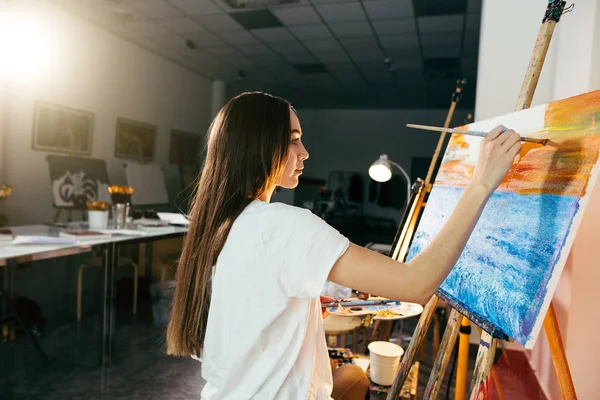 Nő művész festeni egy képet a festőállvány olajjal fest neki a műhelyben — Stock Fotó