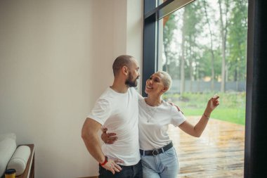 Genç evli bir çift apartmanın penceresinden bakıyor.