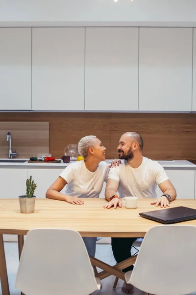Belo casal caucasiano sentado na mesa em casa, sorrindo juntos — Fotografia de Stock