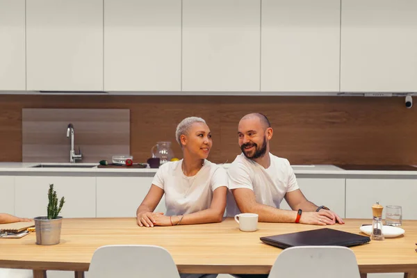 Hermosa pareja caucásica sentado en la mesa en casa, sonriendo juntos — Foto de Stock