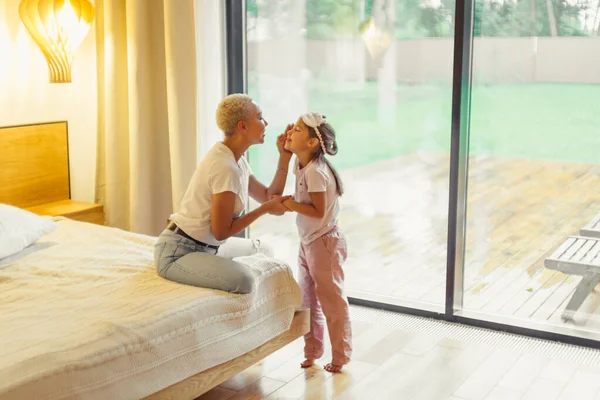 Mamma accarezzando adorabile piccola figlia seduta sul letto — Foto Stock