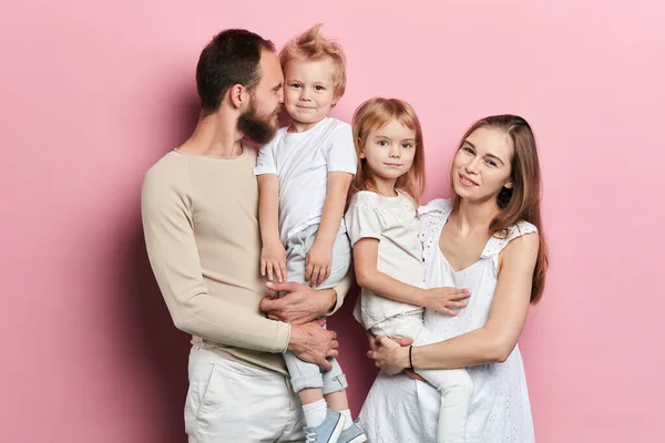 Jovem família feliz com adoravle filhinhas posando no fundo rosa — Fotografia de Stock