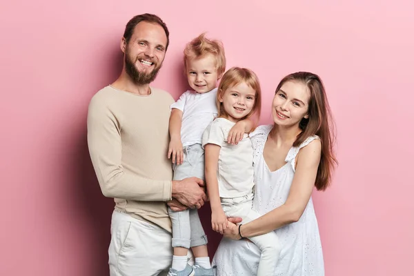 Jovem família feliz com adoravle filhinhas posando no fundo rosa — Fotografia de Stock