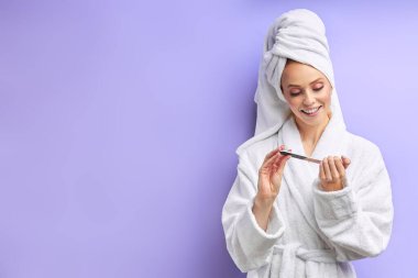 Bornoz giymiş mutlu beyaz kadın tırnaklarını kesiyor.