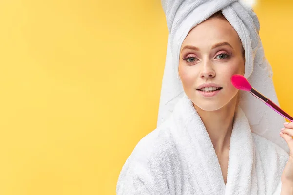Zbliżenie piękna kobieta robi makijaż z za pomocą pędzla izolowane na żółtym tle — Zdjęcie stockowe