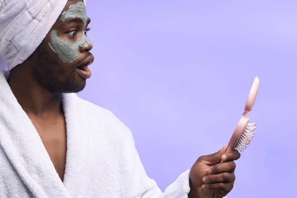 Atractivo hombre negro con máscara de belleza para la cara mira el espejo —  Fotos de Stock