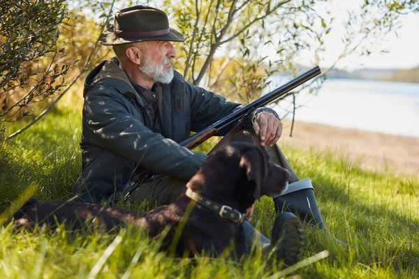 Senior-Jäger ruht sich mit Hund aus, sitzt auf Gras — Stockfoto