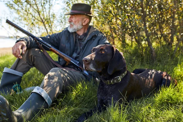 Caçador caucasiano maduro sentado com cão na grama — Fotografia de Stock