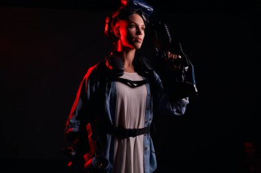 Genç bayan sanal gerçeklik kulaklığı ve karanlık dumanlı odada silah kullanarak oyun oynuyor.