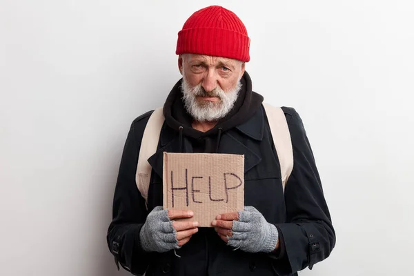 Poor old-aged bum in red hat and street wear holding cardboard sign — Stock Photo, Image