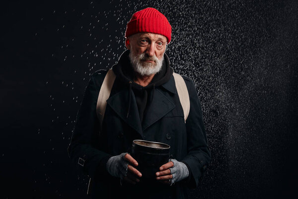 Old beggar man in street clothes stand under rain