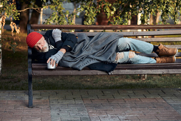 Poor homeless man lying on bench in cold weather