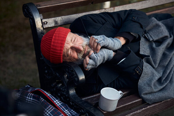 View of frozen old man lying on bench in city park in cold weather