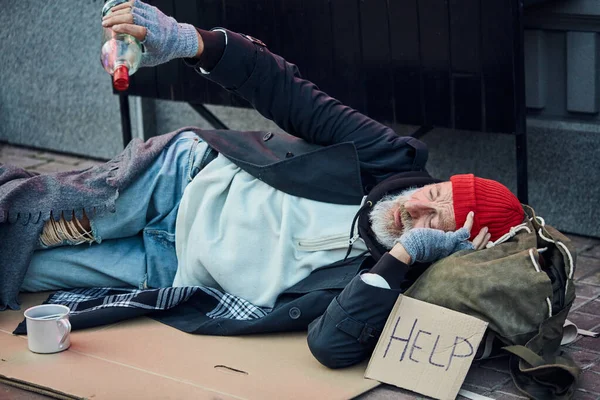 Disperato mendicante in vecchi vestiti sdraiato su una scatola di cartone — Foto Stock