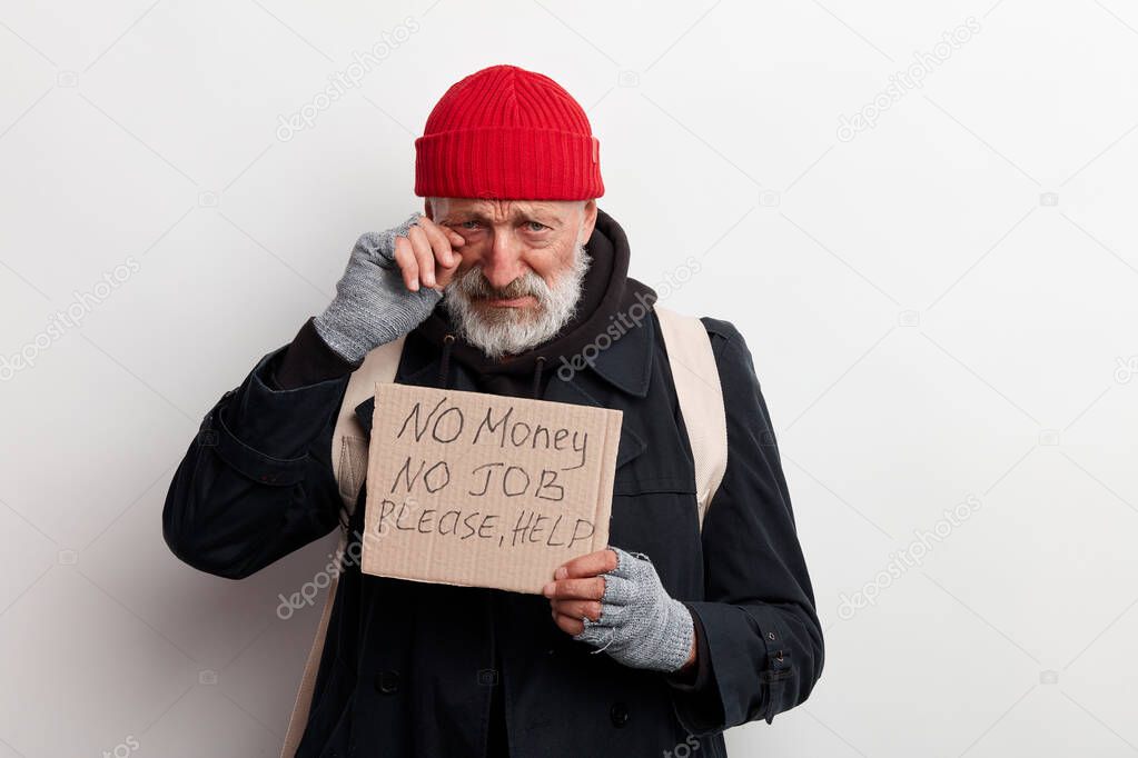 Poor old-aged bum in red hat and street wear holding cardboard sign
