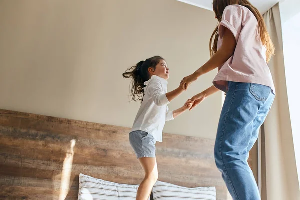 Glückliche Frau springt mit Tochter auf Bett — Stockfoto