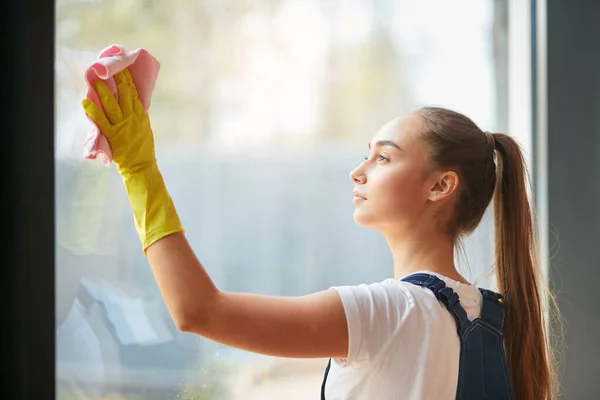 Концепция домашнего хозяйства. Молодая девушка в перчатках моет большое окно — стоковое фото