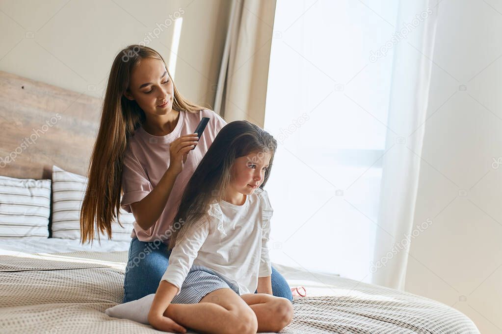 Kind charming mother doing hairstyle