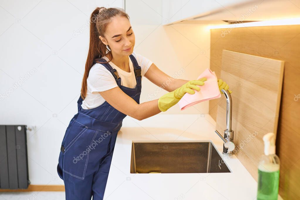 Attractive janitor in working uniform cleaning kitchen