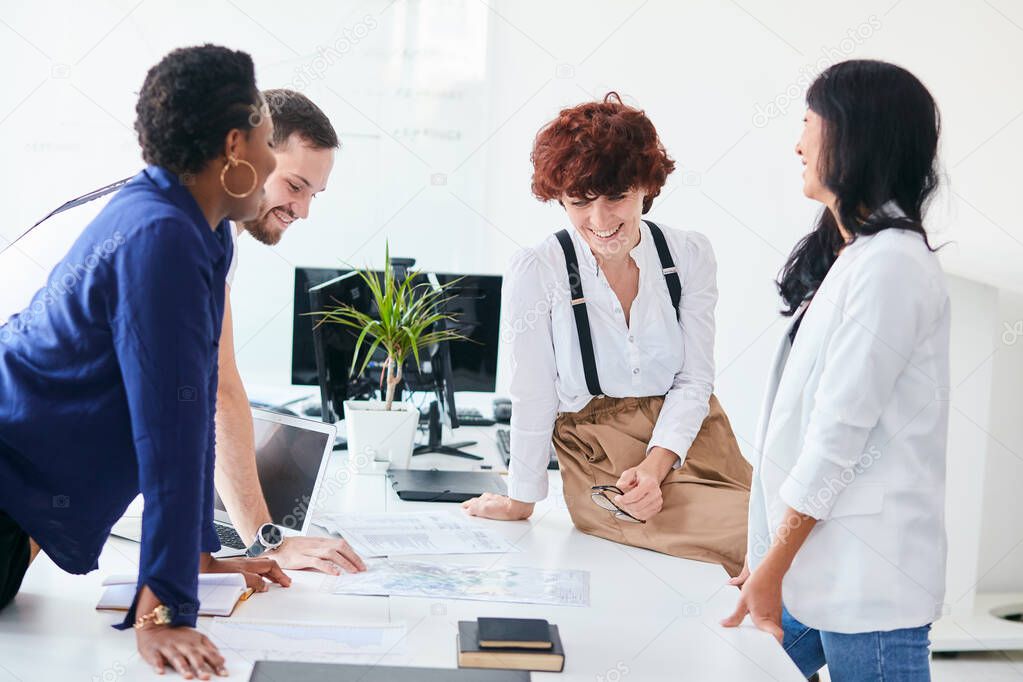 Excited multiracial people sitting at shared office desk laugh joking