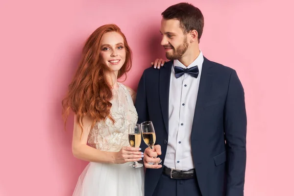 Smiling wedding couple with champagne isolated over pink background — Stock Photo, Image