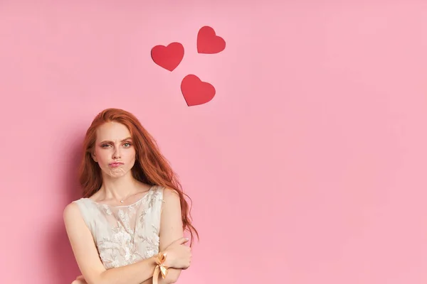 Жінка з рудим волоссям на рожевому тлі з сердечками — стокове фото