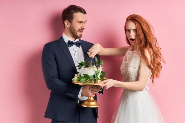 Casal surpreso segurando bolo doce isolado sobre fundo rosa — Fotografia de Stock