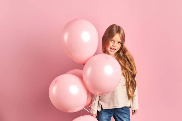 Портрет веселой маленькой девочки на розовом фоне, держащей кучу розовых воздушных шаров — стоковое фото