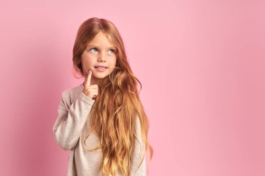 Düşünceli küçük kız pembe arka planda tek başına hayal kuruyor.