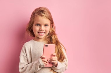 Pembe arka planda izole edilmiş akıllı telefonlu sevimli bir kızın portresi.