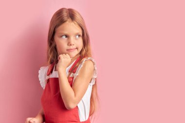 Pembe arka planda izole edilmiş kırmızı tulumlu rüya gibi küçük kız.