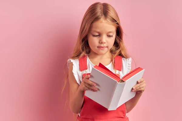 Menina atenta ler atentamente livro isolado sobre fundo rosa — Fotografia de Stock