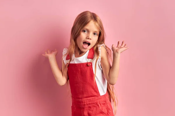 Joyful klein meisje in rode overall geïsoleerd op roze achtergrond — Stockfoto