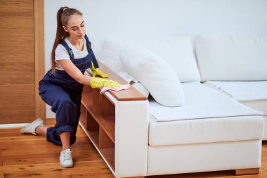 Koruyucu lastik eldivenli kadın hademe kanepenin tozunu siliyor.