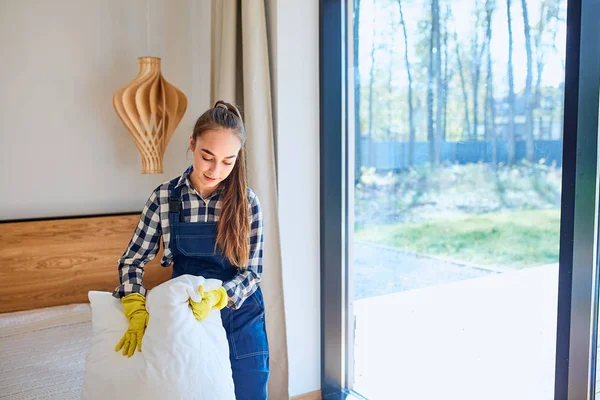 Young woman janitor making bed in living room — Stock Photo, Image