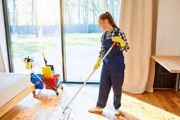 Donna cameriera in uniforme blu pulizia pavimento in camera da letto — Foto Stock