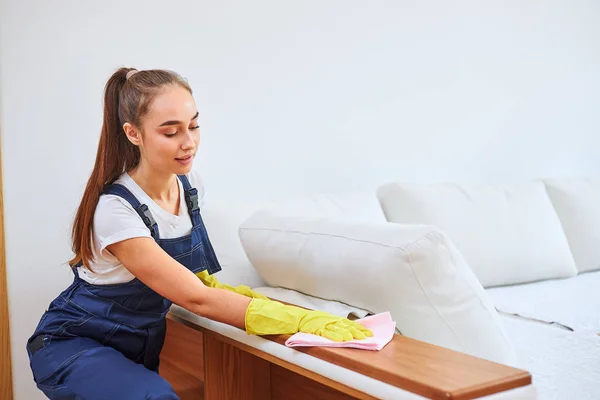 Snygg kvinna i blå uniform städa upp rum, soffa — Stockfoto