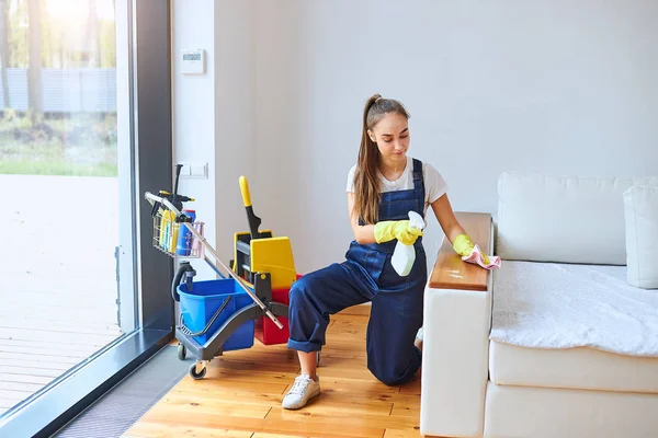 Putzfrau sitzt neben Sofa und wischt Staub weg — Stockfoto