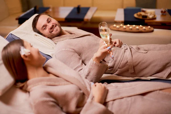 Любящие кавказскую молодую пару пьют шампанское в спа-центре — стоковое фото