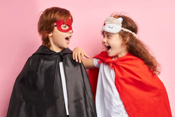 Pelerinli ve maskeli çocuklar pembe arka planda izole edilmiş.