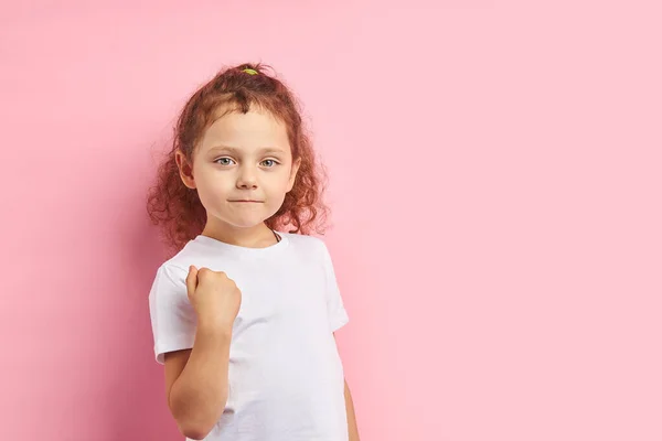 Gefährliches Mädchen 5-6 Jahre mit lockigem kastanienbraunem Haar isoliert über rosa Hintergrund — Stockfoto