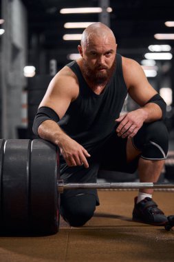 Halterin yanında oturan vücut geliştirici.