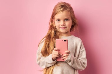 Tatlı küçük kız pembe arka planda izole edilmiş ellerde cep telefonunu tutuyor.