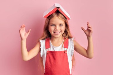 Kafasıyla ilgili kitabı pembe arka planda olan oyuncu beyaz kız.