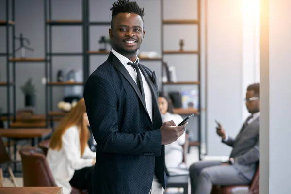 Portret van succesvolle en lachende jonge Afrikaanse zakenman met mobiele telefoon in functie — Stockfoto