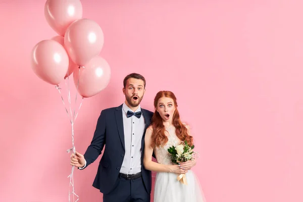 Retrato de casal jovem casamento surpreso de pé isolado sobre fundo rosa — Fotografia de Stock